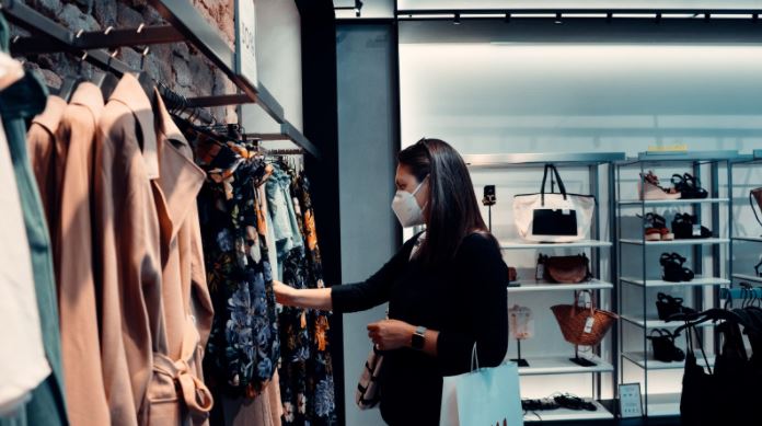 Person shopping in a high-street store looking at clothes and wearing a face mask.