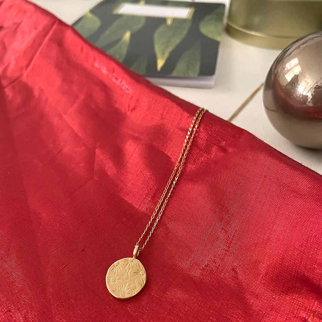 a gold textured necklace is lying on top of a shiny red fabric