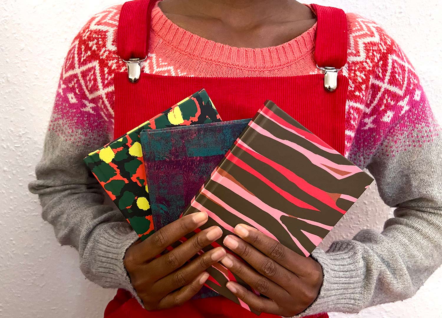 a model holds three notebooks fanned out in different colourful patterns 
