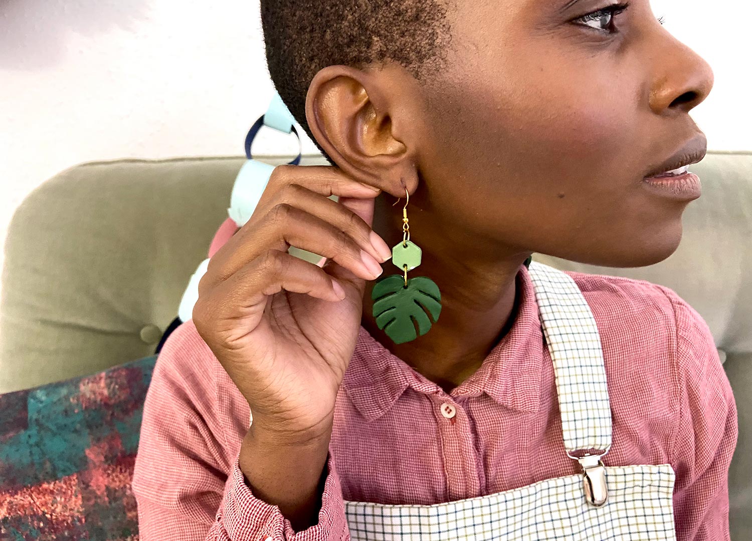A model holds her hand up to her ear, she wears green clay earrings with a monstera leaf