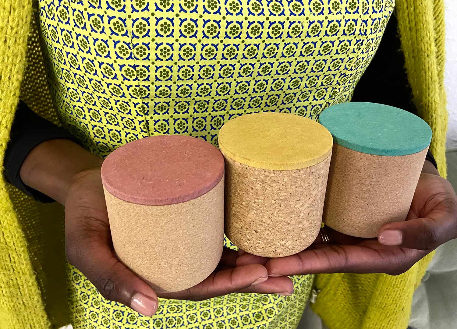 close up of a model holding three cork vessels with different colour lids 