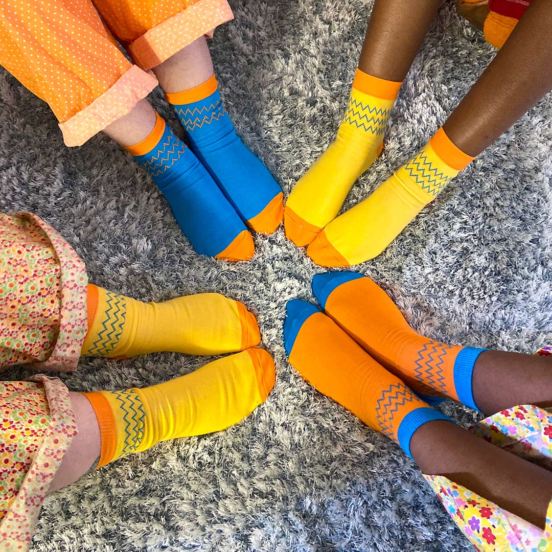 four pairs of feet wear brightly coloured socks, toes pointing towards the middle