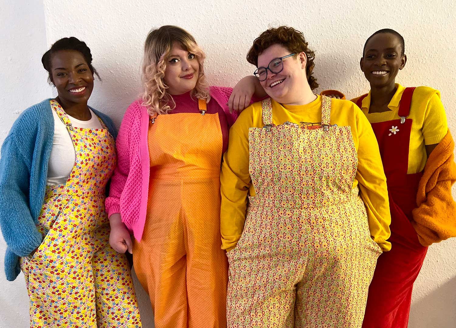 four models stand looking at the camera and smiling, wearing pairs of brightly coloured dungarees, tees and knits.