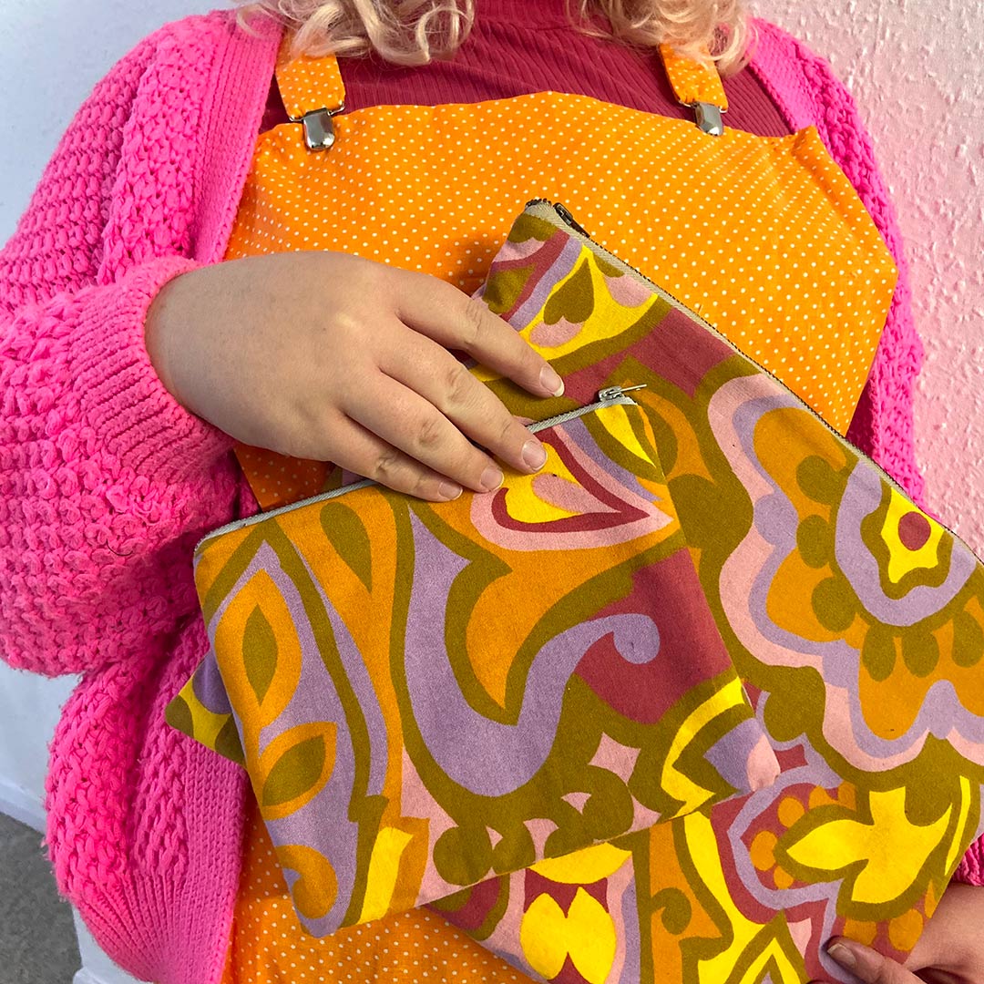 a model wearing orange dotty dungarees holds two brightly coloured zip pouches
