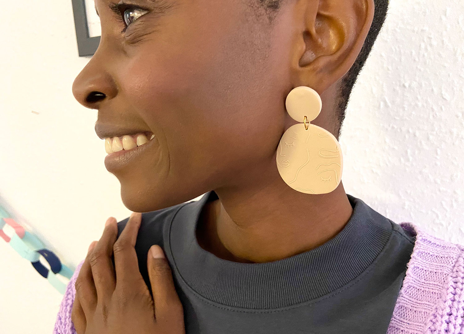 a model wears a large beige earrings with a face design printed in them 